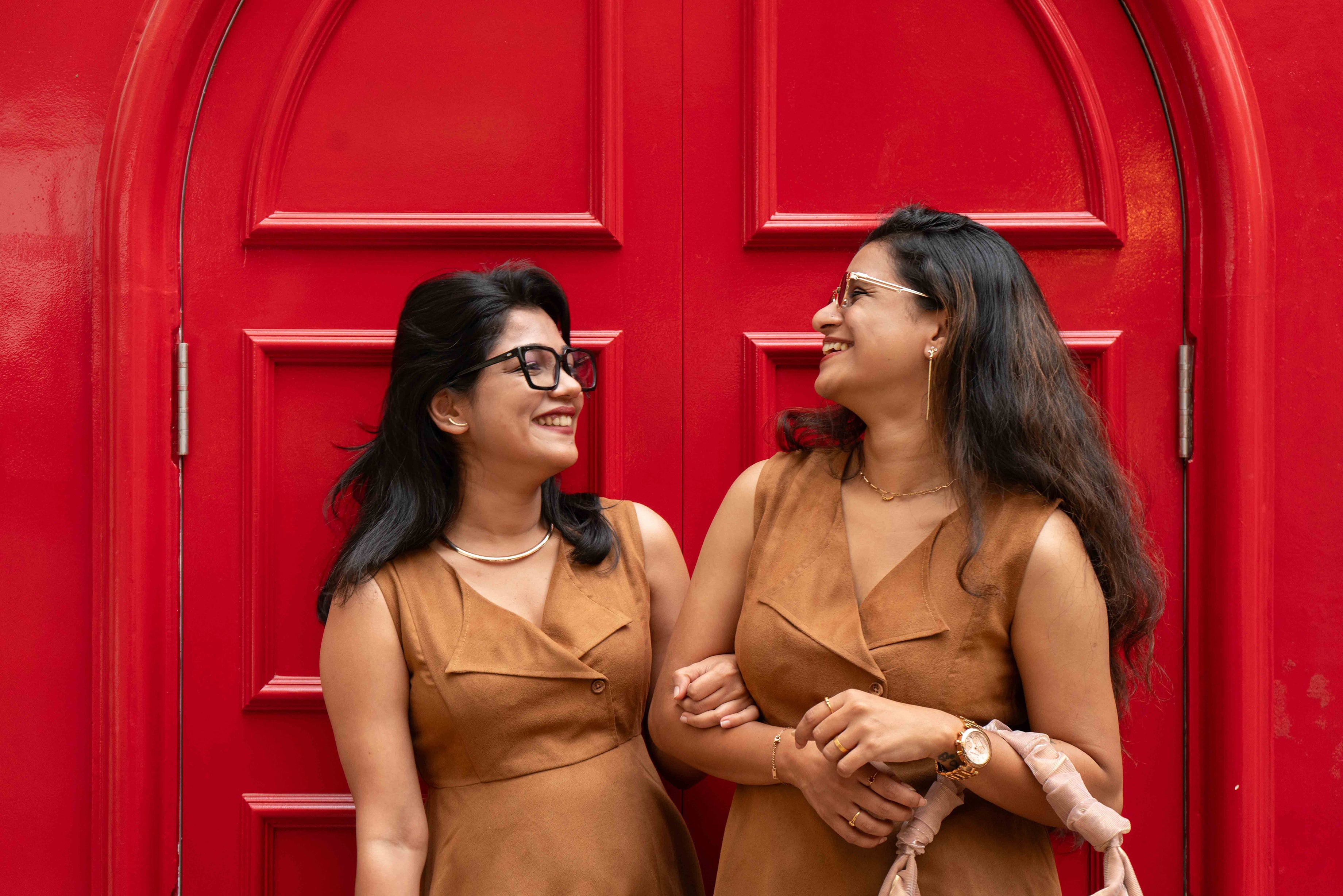 Two women in Toffee suede statement collared dress standing in front of a red door, smiling and laughing.