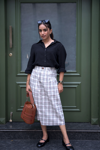Woman standing in front of a green door wearing a smart casual work wear boardroom basic black shirt and dawn pleated plaid skirt.