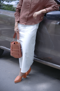 Women wearing a smart casual work wear white lady diana skirt and mocha brown shirt with orange shoes, holding a brown bag, standing next to a car.