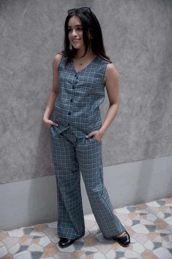 Woman wearing a smart casual work wear old school checks vest and 9 to 9 pant standing against a grey wall.