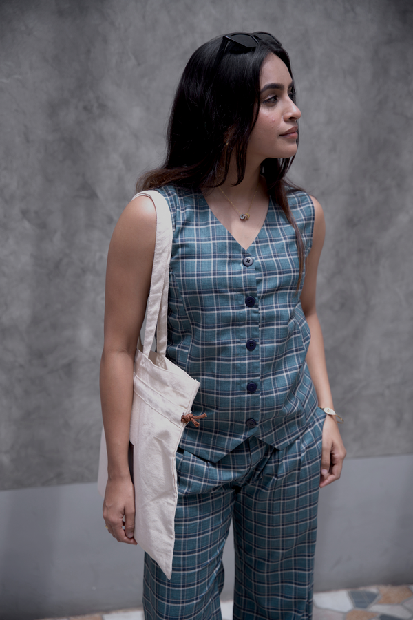Woman wearing a smart casual work wear old school checks plaid vest and 9 to 9 pants with a Mate tote bag against a gray background