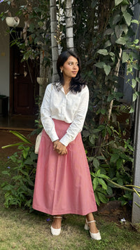 Woman in a smart casual work wear white clean slate shirt and red pin check skirt standing outdoors among plants.